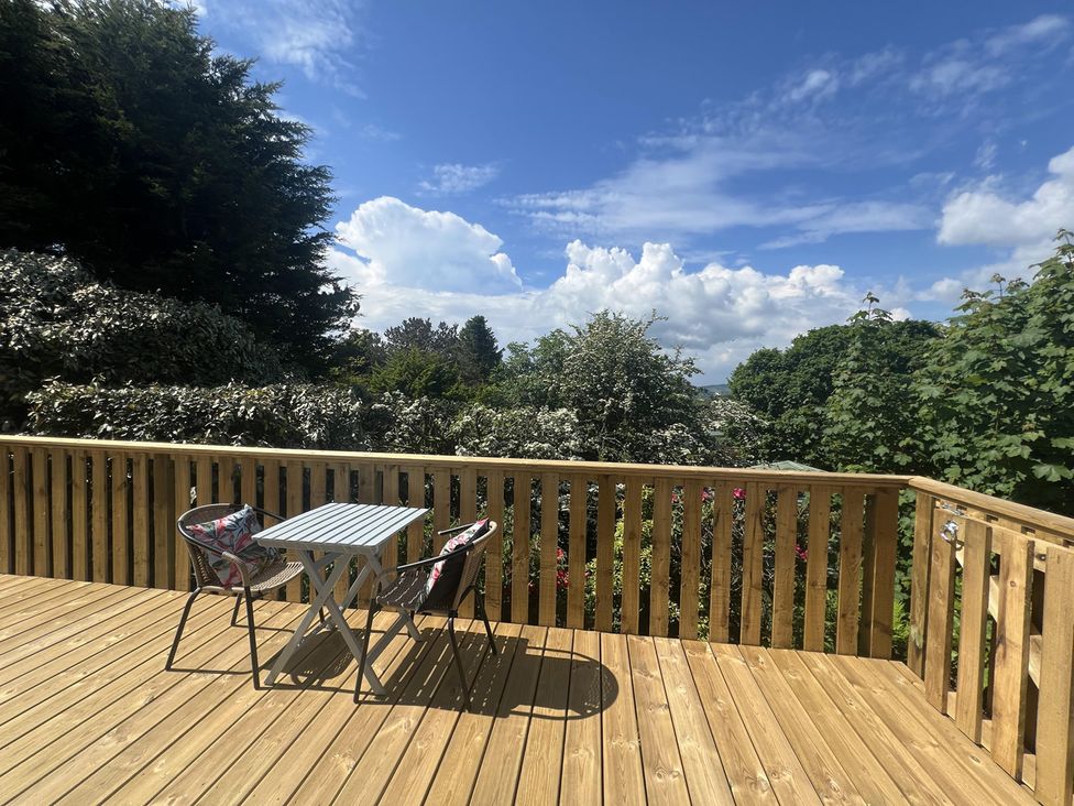 A deck with a table and chairs overlooking greenery at Holly Blue - Cosy wooden lodge, Kippford