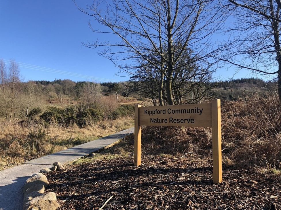 A sign for Kippford Community Nature Reserve with a pathway in Kippford Holiday Park near Dalbeattie