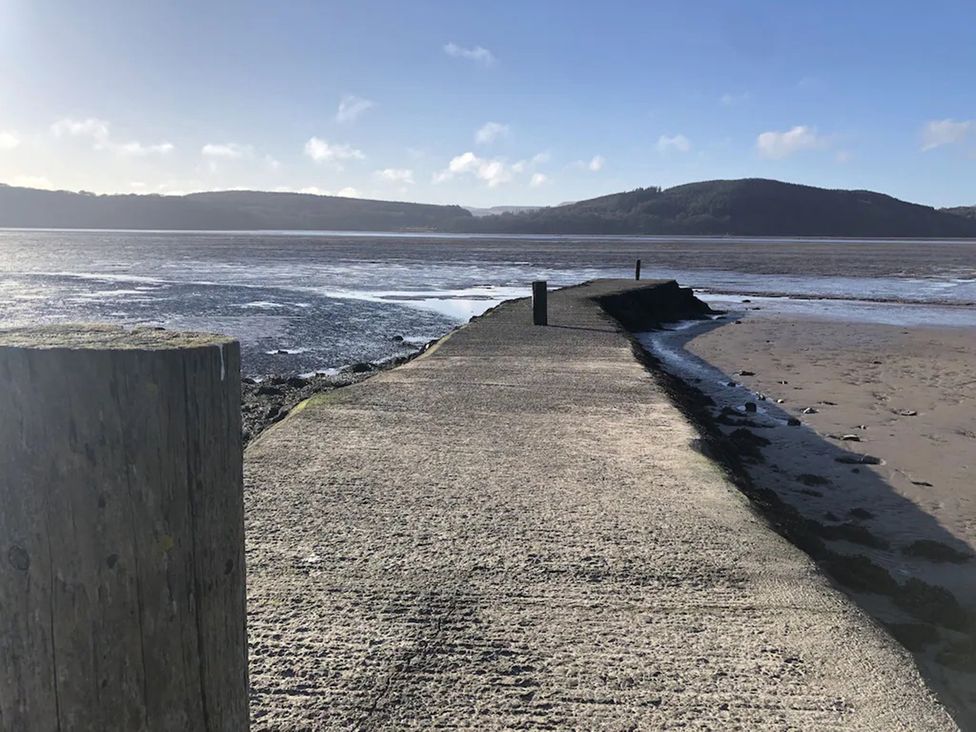 A concrete walkway along a river with wooden posts at Holly Blue - Cosy wooden lodge, Kippford