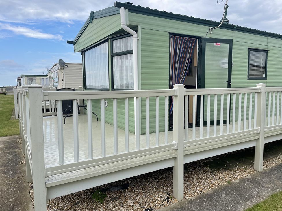 A caravan with a deck and railing at 4 Bed Lodge Sleeps 8 - Pets & WiFi Free Parking in Ingoldmells