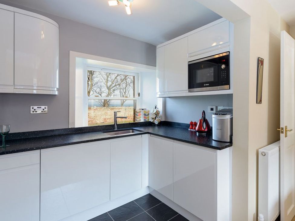 A kitchen with cabinets, sink, microwave, and a window at Charming Cottage in North Berwick