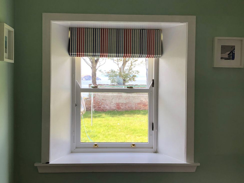 A window with a striped curtain overlooking grass and trees at Charming Cottage in North Berwick