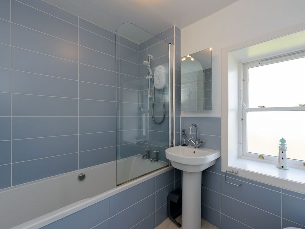 A bathroom with a bathtub, shower, sink, and window at Charming Cottage in North Berwick