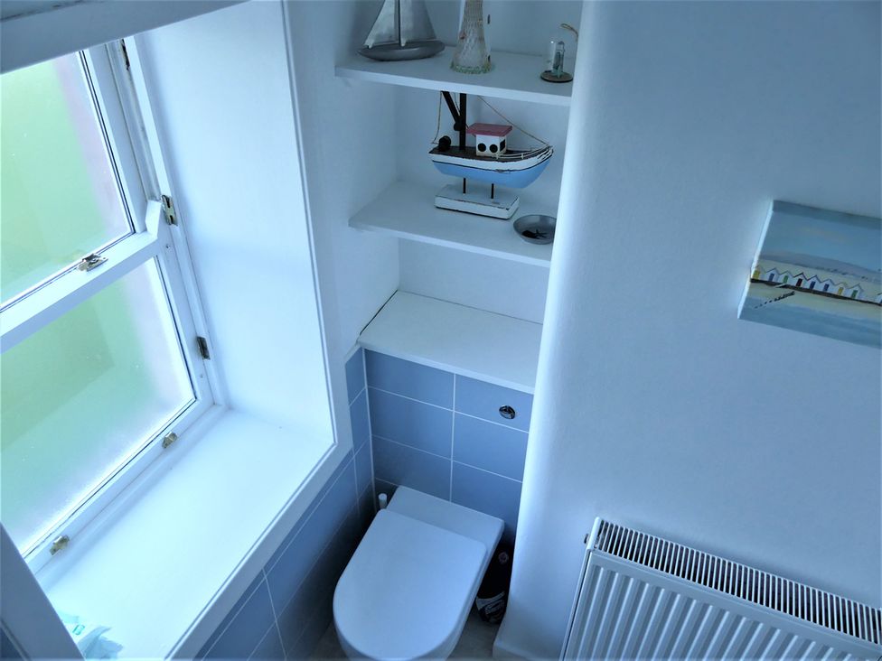 A bathroom with a toilet and a shelf with a boat decorative item at Charming Cottage in North Berwick