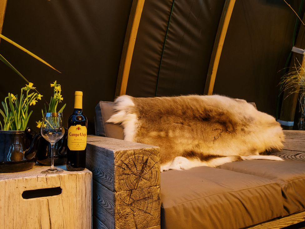 A couch with a faux fur throw and wine at Shepherd's Hut- Hot Tub- Wellness Spa- Wood Burner Nottingham