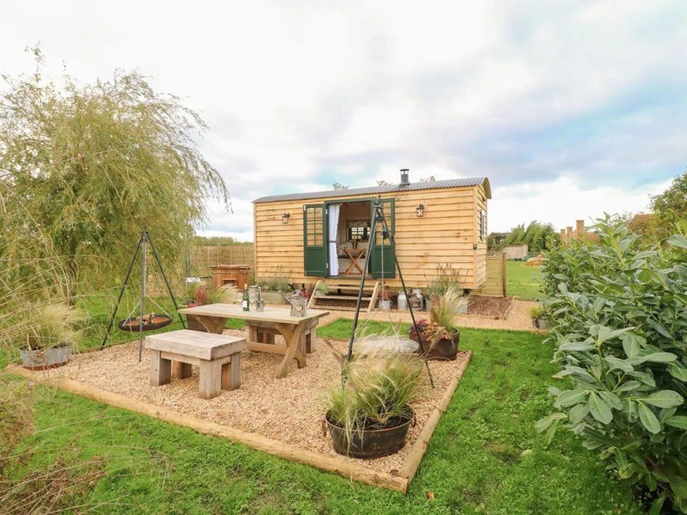 A wooden cabin with a table and swing set at Shepherd's Hut- Hot Tub- Wellness Spa- Wood Burner Nottingham