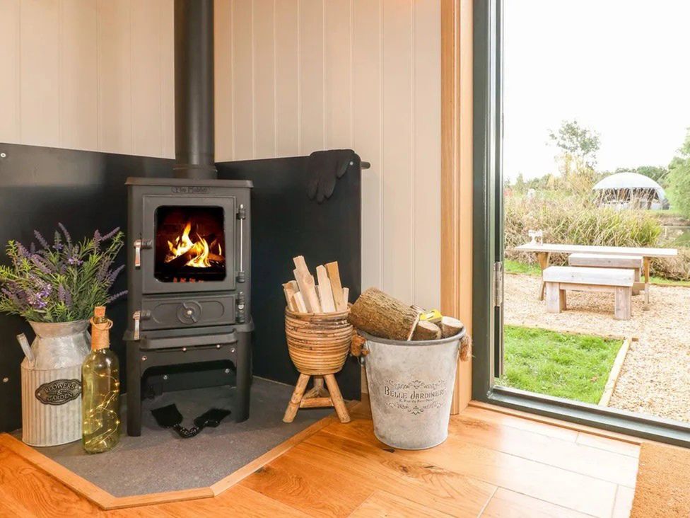 A cozy indoor area with a wood burner and firewood at Shepherd's Hut- Hot Tub- Wellness Spa- Wood Burner Nottingham