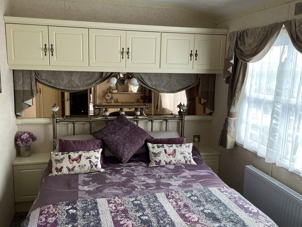A bedroom with a bed and decorative cushions at Chalet Sleeps 4 Near Cymyran Beach Caergeiliog
