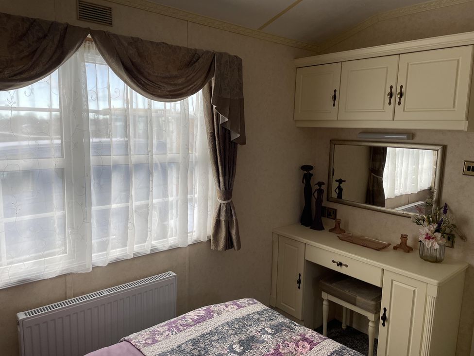 A bedroom with a window and a mirror at Chalet Sleeps 4 Near Cymyran Beach Caergeiliog