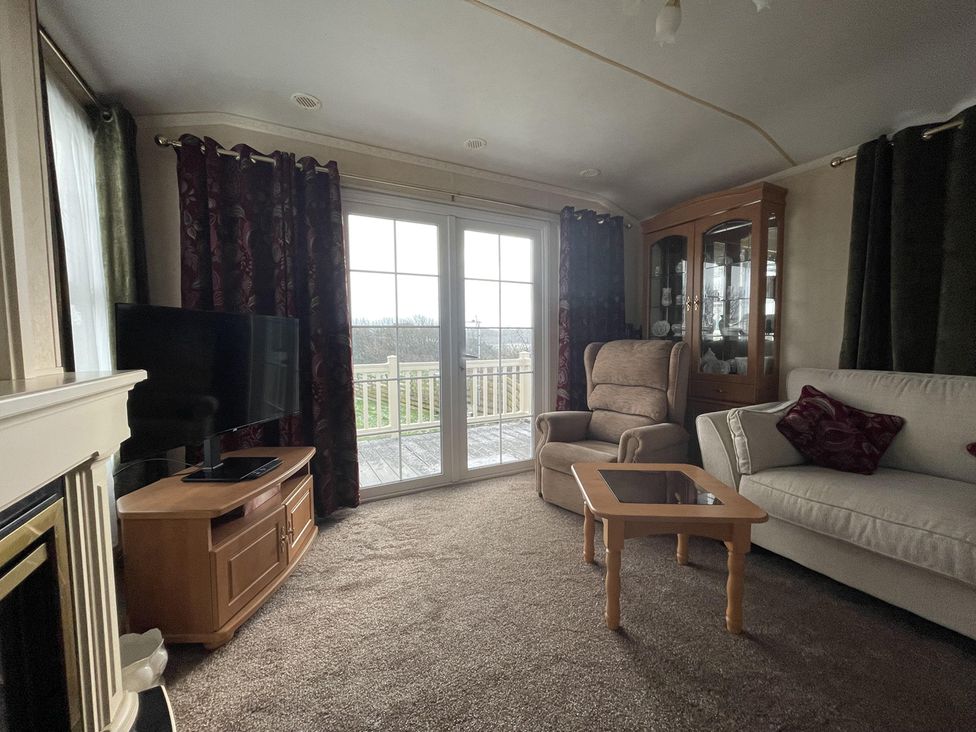 A living room with a television and sliding door at Chalet Sleeps 4 Near Cymyran Beach in Caergeiliog