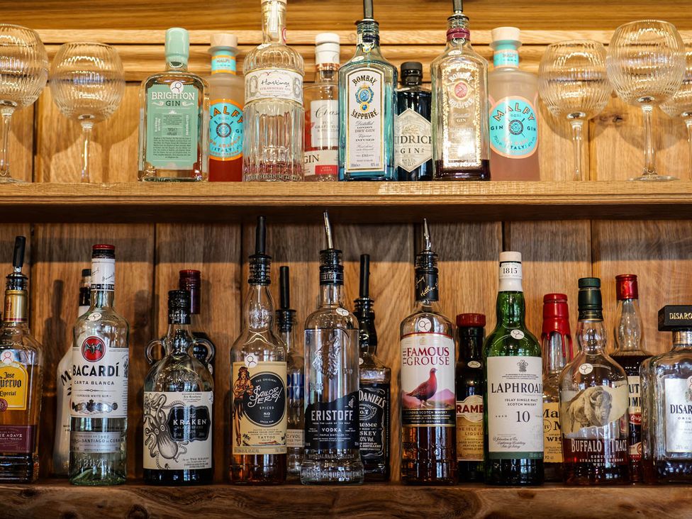 A bar shelf with various bottles of spirits and glasses at Royal Oak Retreat Sleeps 6 Pub Pet Friendly Barcombe Cross