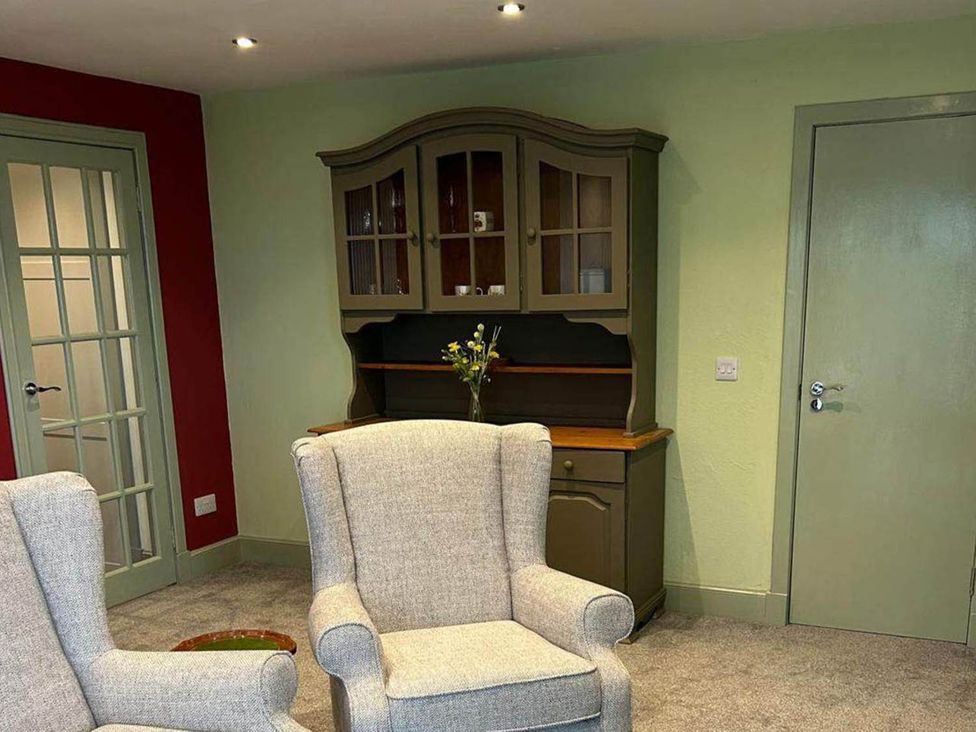 A living room with an armchair and display cabinet at Marsco Apartment Garden Patio Sea Views Applecross near Lochcarron