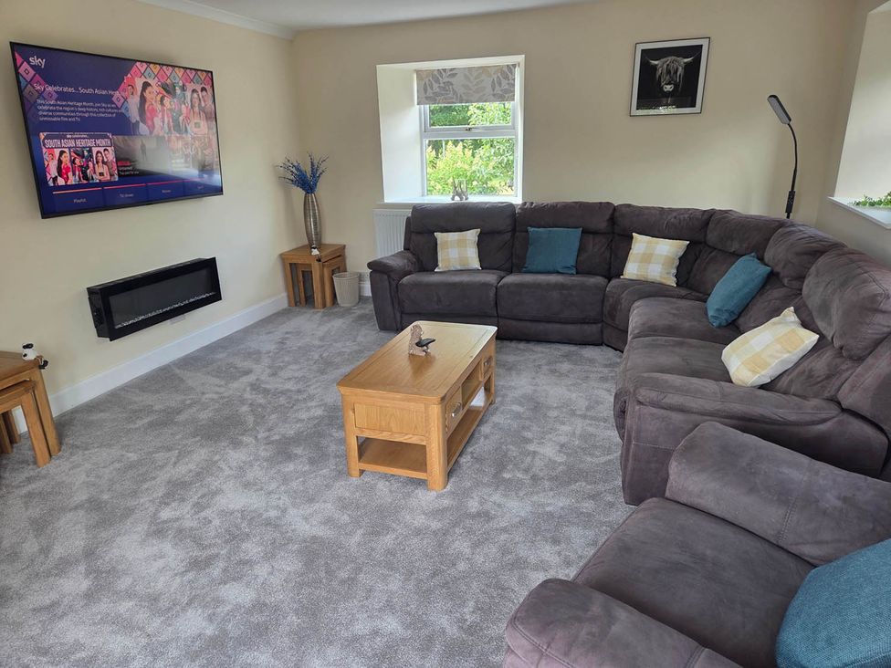 A living room with a large sofa, coffee table, and television at Farm Cottage at foot Angus Glens, Kirkton of Kingoldrum near Kirriemuir