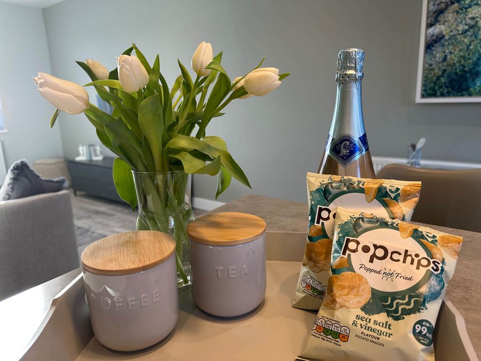 A table with jars of coffee and tea, a bottle, popchips, and flowers at Stylish Home Sleeps 4 Free Parking, Earl Shilton