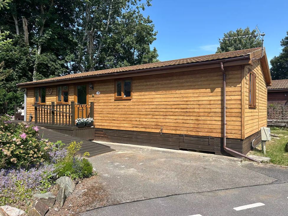 A wooden cabin with porch and garden flowers at Cabin Sleeps 4 with Hot Tub and Parking Near Wilberfoss