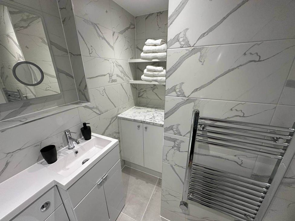 A bathroom with a sink, mirror, shelves, and towels at 59 Whitstable - One Bedroom Ground Floor Flat, Whitstable