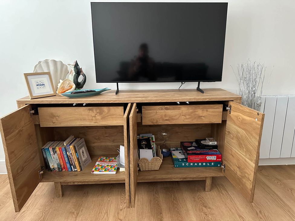 A television on a wooden table with books and games at 59 Whitstable - One Bedroom Ground Floor Flat, Whitstable