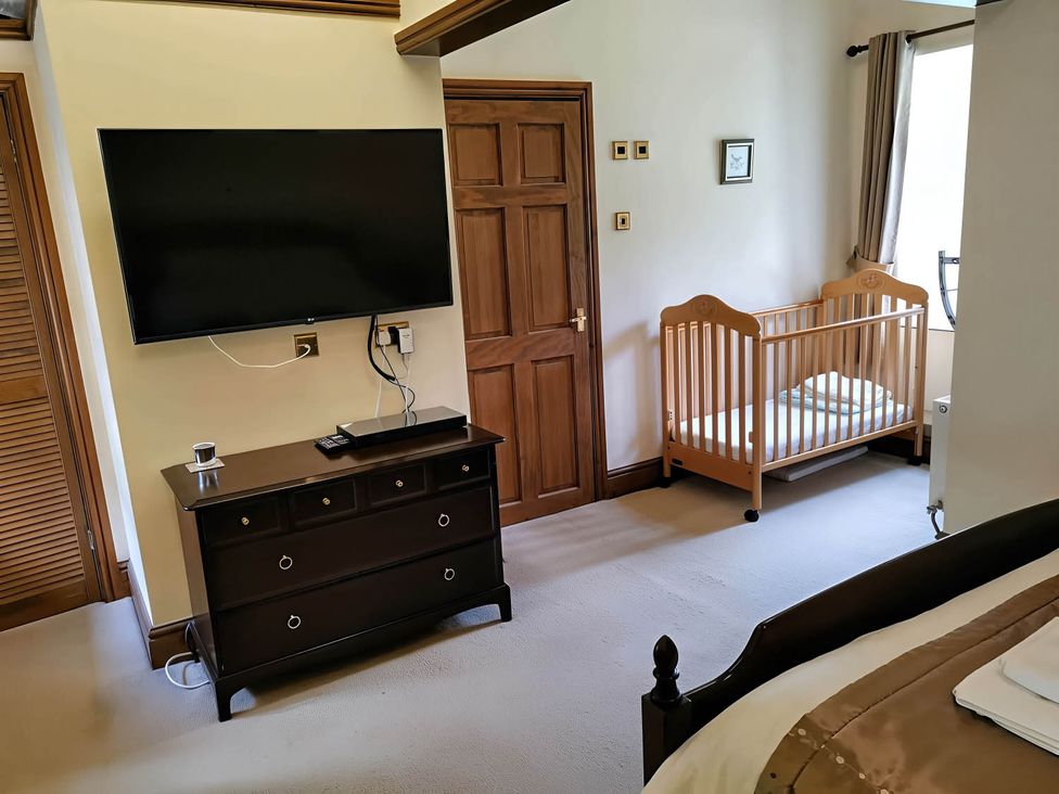 A bedroom with a crib and television at The Old Barn in Barmouth