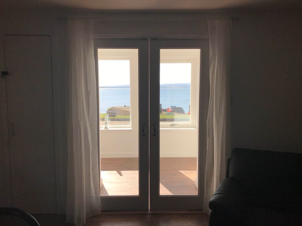 A living room showing doors and a window overlooking the sea at PetFriendly Beachfront Sunset Facing Porch Garden in Portmahomack