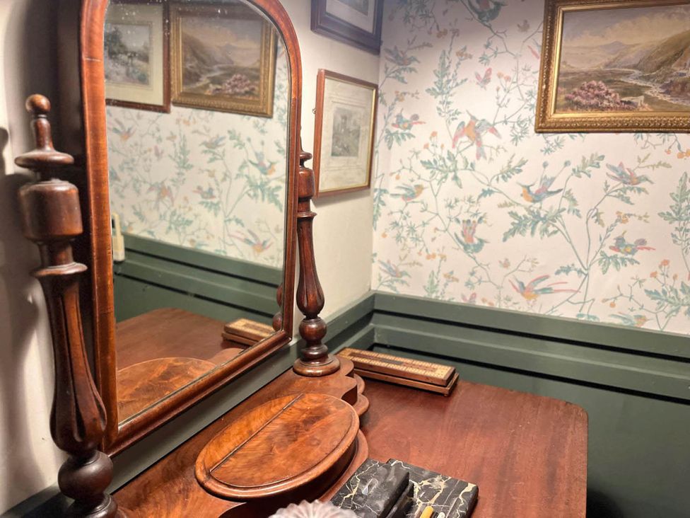 A wooden dressing table with a mirror and paintings on the wall at The Old Barn in Bovey Tracey