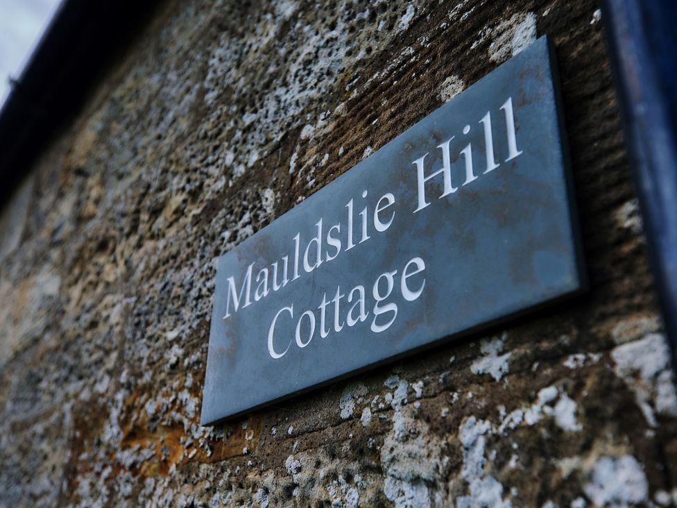 A sign on a stone wall reading Maudslie Hill Cottage near Edinburgh