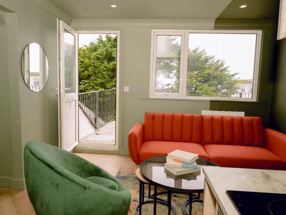 A living room with a red sofa, green armchair, and table at 1 Bedroom Apartment, sleeping 3 with balcony and pet friendly, Carbis Bay