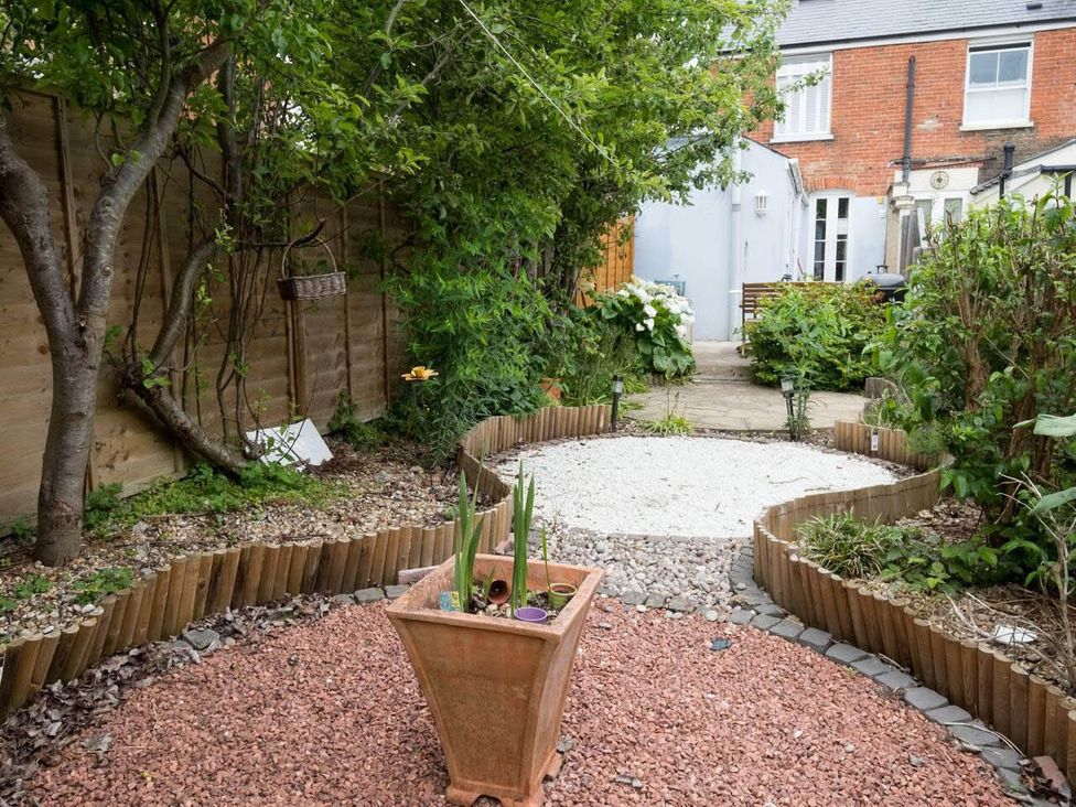 A garden with a gravel path, plant pot, and trees at Impeccable 3 bed 2 bath Central Cowes Cottage Cowes