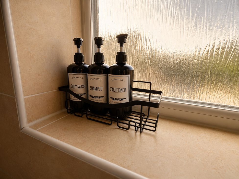 A bathroom with body wash, shampoo, and conditioner on a shelf at Family Friendly Coach House - Parking - Sleeps 4 Ebdon