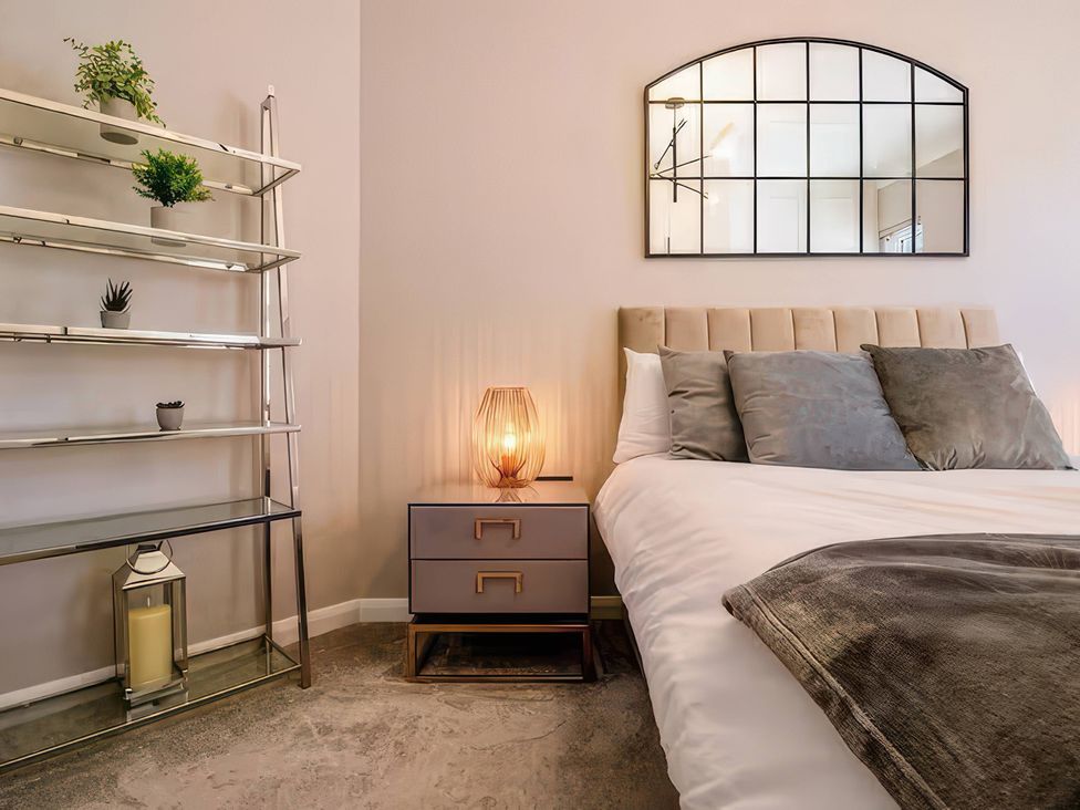 A bedroom with a bed, nightstand, lamp and shelf at 7 Wolsey Mansions, Northwood, Hertfordshire