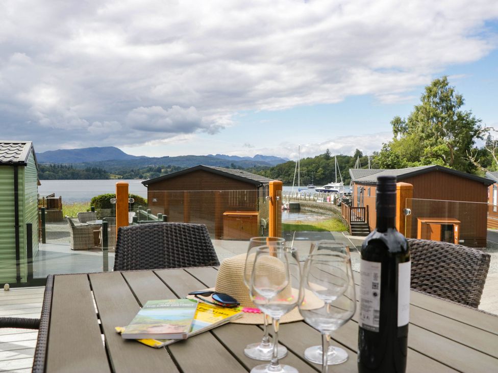 An outdoor area with a table, glasses, and a view of water and cabins at 19 Pony Meadow White Cross Bay near Troutbeck Bridge