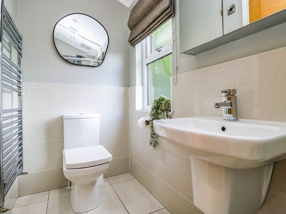 A bathroom with a toilet, sink, mirror, and towel radiator at 19 Pony Meadow White Cross Bay near Troutbeck Bridge