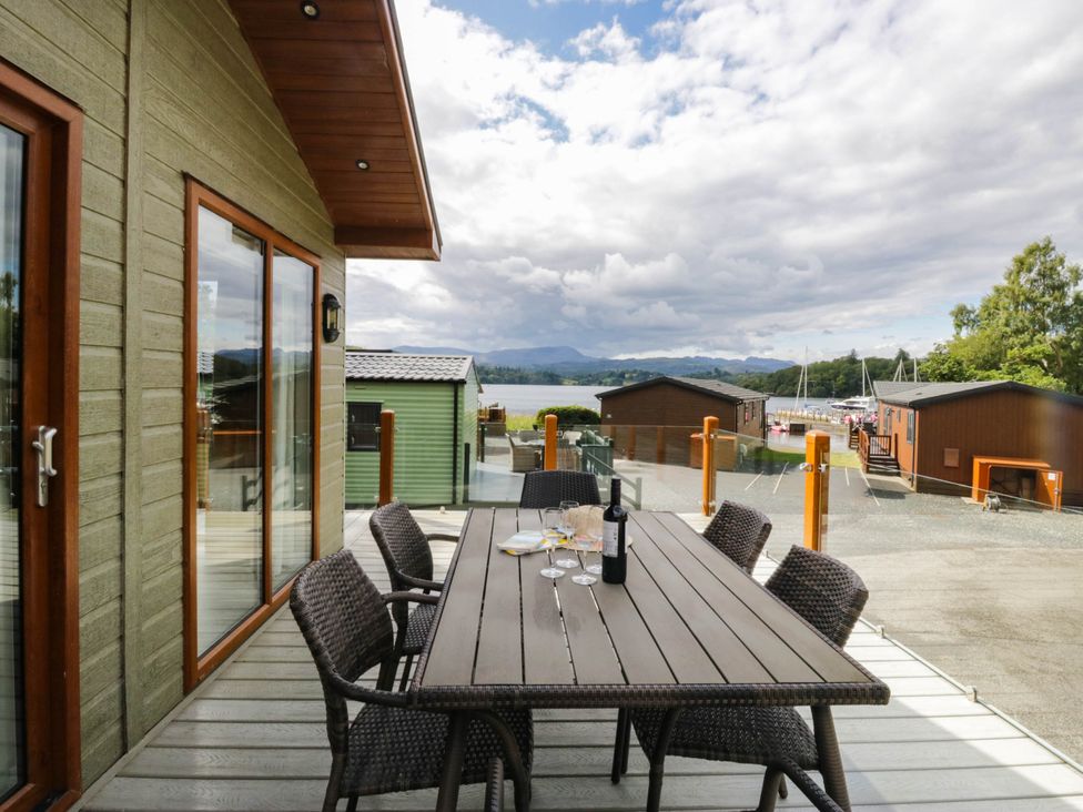 An outdoor dining area with a table and chairs overlooking a lake at 19 Pony Meadow White Cross Bay near Troutbeck Bridge