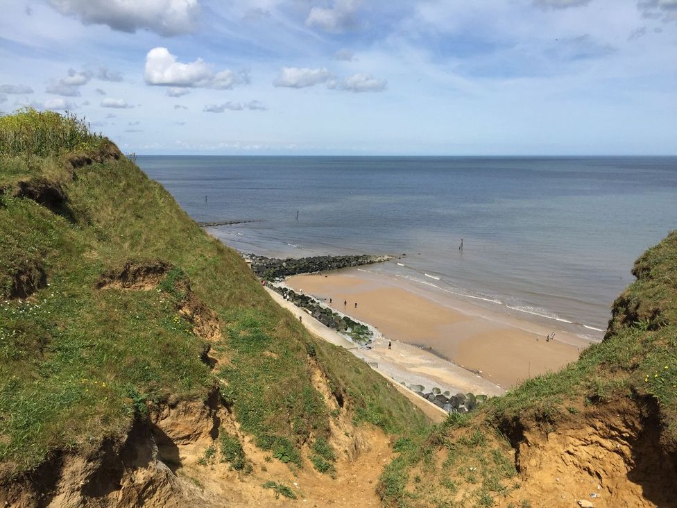A beach view from a cliff with grass and rocks at Beck Cottage in Sheringham