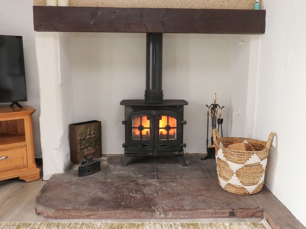A fireplace with a wood stove and a basket of logs at The Thatched Cottage in Preston
