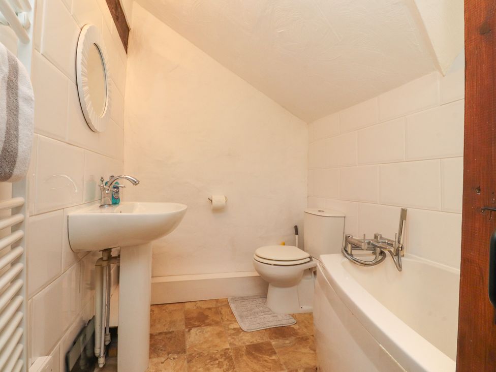 A bathroom with a sink, toilet, bathtub, and mirror at The Thatched Cottage in Preston