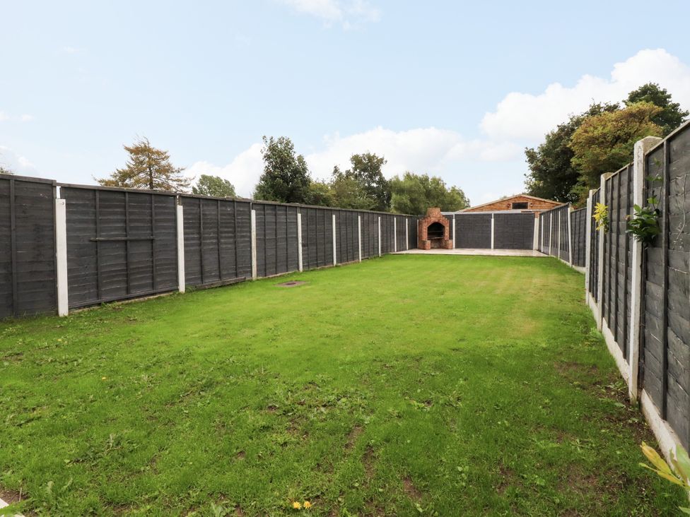An outdoor garden with a grassy area and a brick barbecue at The Thatched Cottage Preston