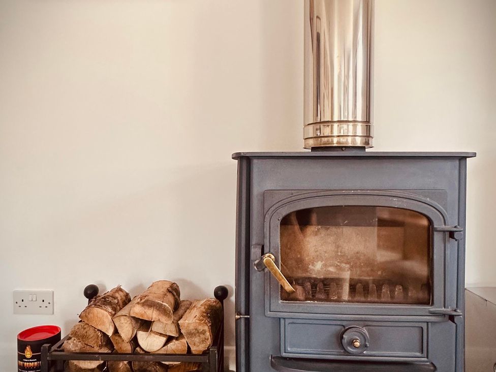A wood stove with logs and a log holder at Muddy Boots – Scarpa Kirkby Stephen