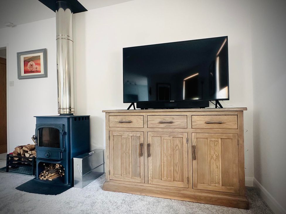 A living room with a television on a cabinet and a wood stove at Muddy Boots – Scarpa in Kirkby Stephen