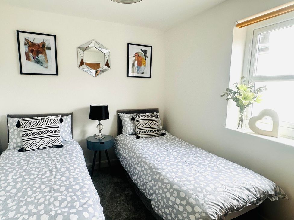 A bedroom with two single beds and a table with flowers at Muddy Boots – Scarpa in Kirkby Stephen
