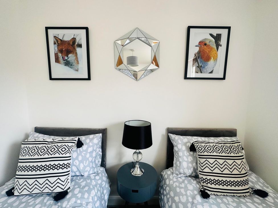 A bedroom with two beds, paintings, and a table lamp at Muddy Boots – Scarpa in Kirkby Stephen