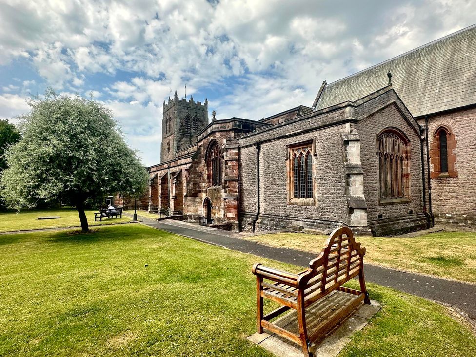 An outdoor view of a church with a tower and benches at Muddy Boots – Scarpa in Kirkby Stephen