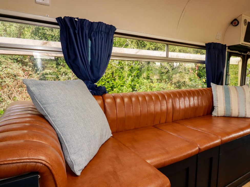 A bus interior with a leather couch and cushions at Honey Bee Bus in Menheniot