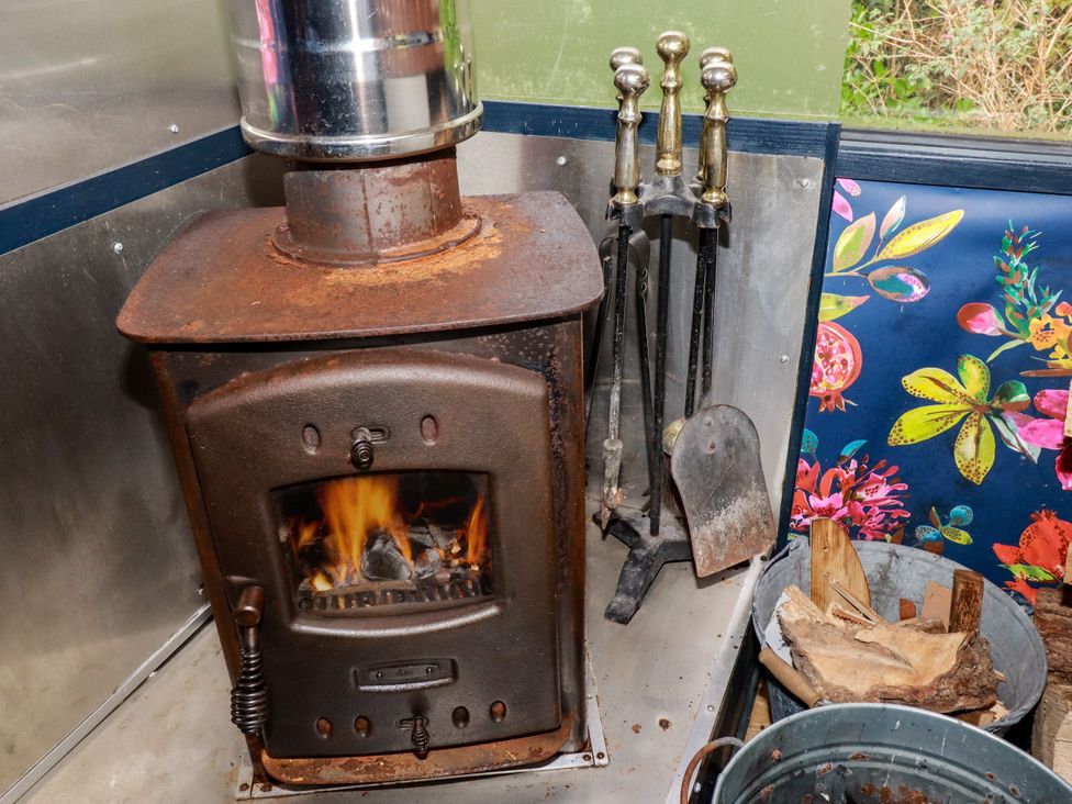A wood stove with firewood and fireplace tools at Honey Bee Bus in Menheniot