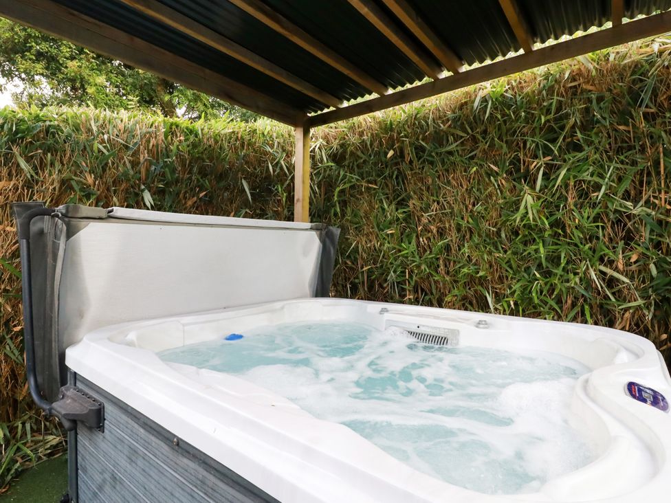 A hot tub under a shelter with surrounding foliage at Honey Bee Bus Menheniot