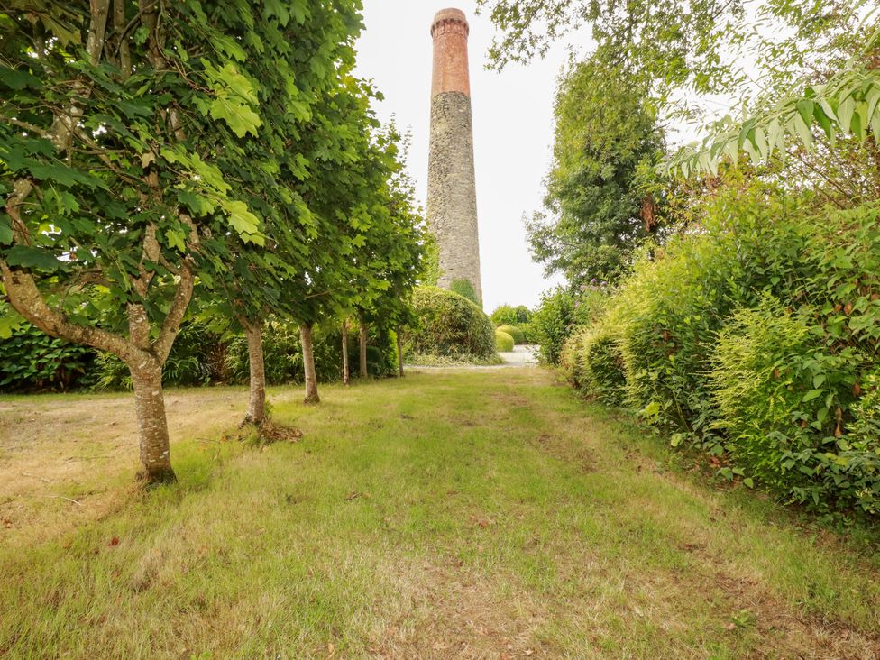 A garden featuring a chimney surrounded by trees and grass at Honey Bee Bus in Menheniot
