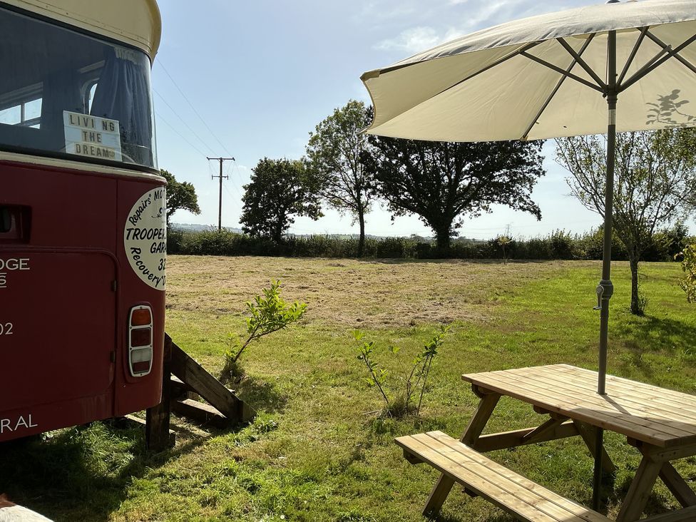 An outdoor area with a red bus, table, and umbrella at Honey Bus in Menheniot
