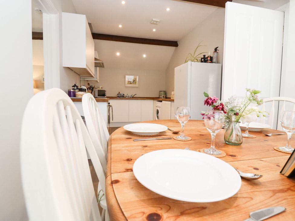 A dining room with a wooden table and kitchen in the background at Peewit Barn in Moreton-in-Marsh