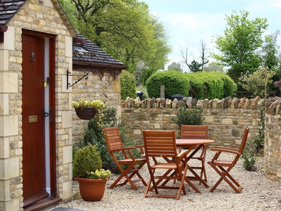 A garden with a stone wall and seating area at Peewit Barn in Moreton-in-Marsh