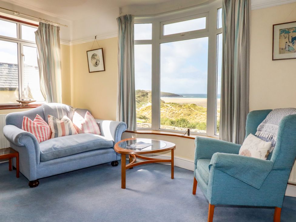 A living room with a sofa and table overlooking the beach at Chy-an-Lowena in Crantock