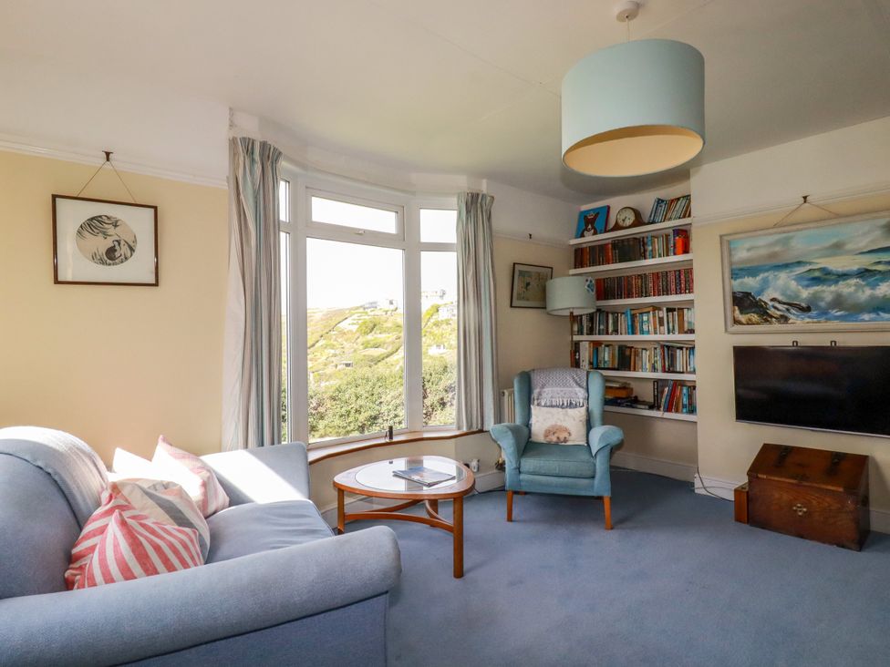 A living room with a sofa, chair, coffee table, bookshelf, and television at Chy-an-Lowena in Crantock